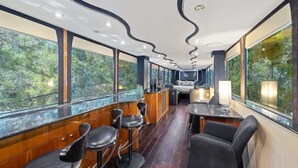 Un intérieur moderne avec un plafond incurvé, de grandes fenêtres offrant une vue sur la verdure et un coin bar avec des tabourets.