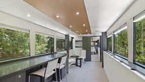 Un intérieur moderne avec un long comptoir, des sièges et de grandes fenêtres offrant une vue sur la verdure.