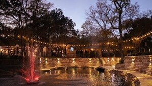 Un espace extérieur aménagé pour la nuit, avec une fontaine, des murs en pierre et des guirlandes lumineuses.