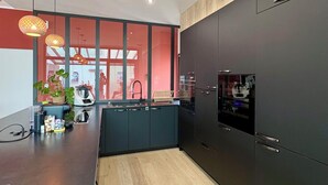 A modern kitchen with dark cabinetry, a wooden floor, and pendant lighting. - villa avec piscine pour 6 personnes proche du théatre antique d'orange (Orange)