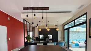 A modern dining area with a long table, white chairs, and pendant lighting. - villa avec piscine pour 6 personnes proche du théatre antique d'orange (Orange)