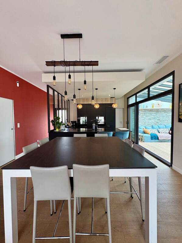 A modern dining area with a long table, white chairs, and pendant lighting.