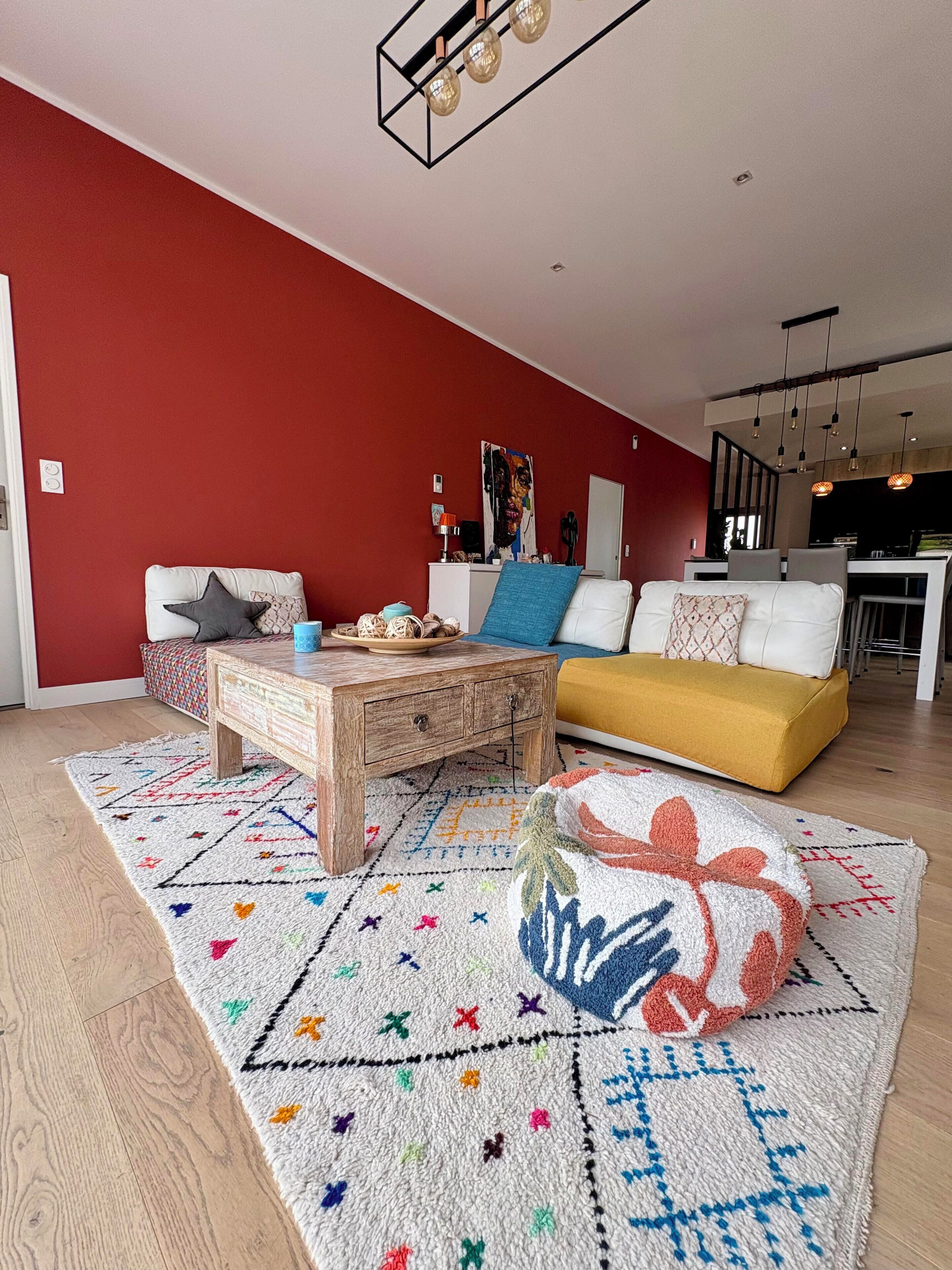 Una sala de estar moderna con una pared de acento roja, una mesa de centro de madera, un sofá amarillo y una alfombra estampada.