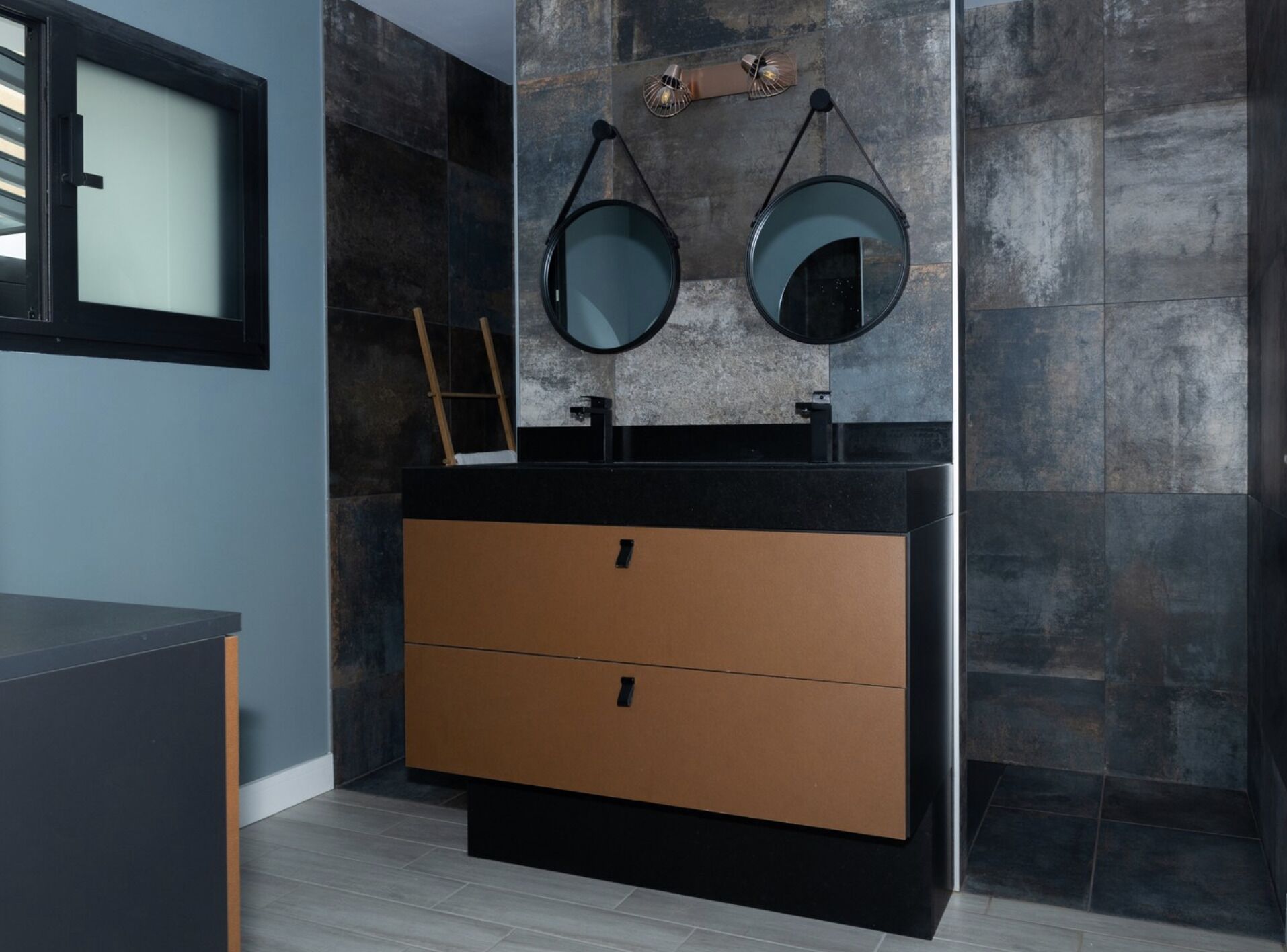 A modern bathroom with a black vanity, two mirrors, and a wooden ladder.