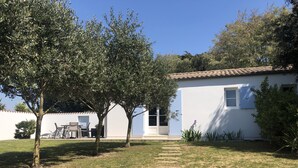 A white building with a tiled roof, a door, and a window. There are trees and a grassy area in front. - LES MIMOSAS (Saint-Pierre-d'Oléron)
