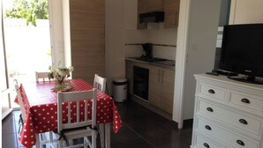 A compact kitchen with a dining area, a TV on a cabinet, and a trash bin. - LES MIMOSAS (Saint-Pierre-d'Oléron)