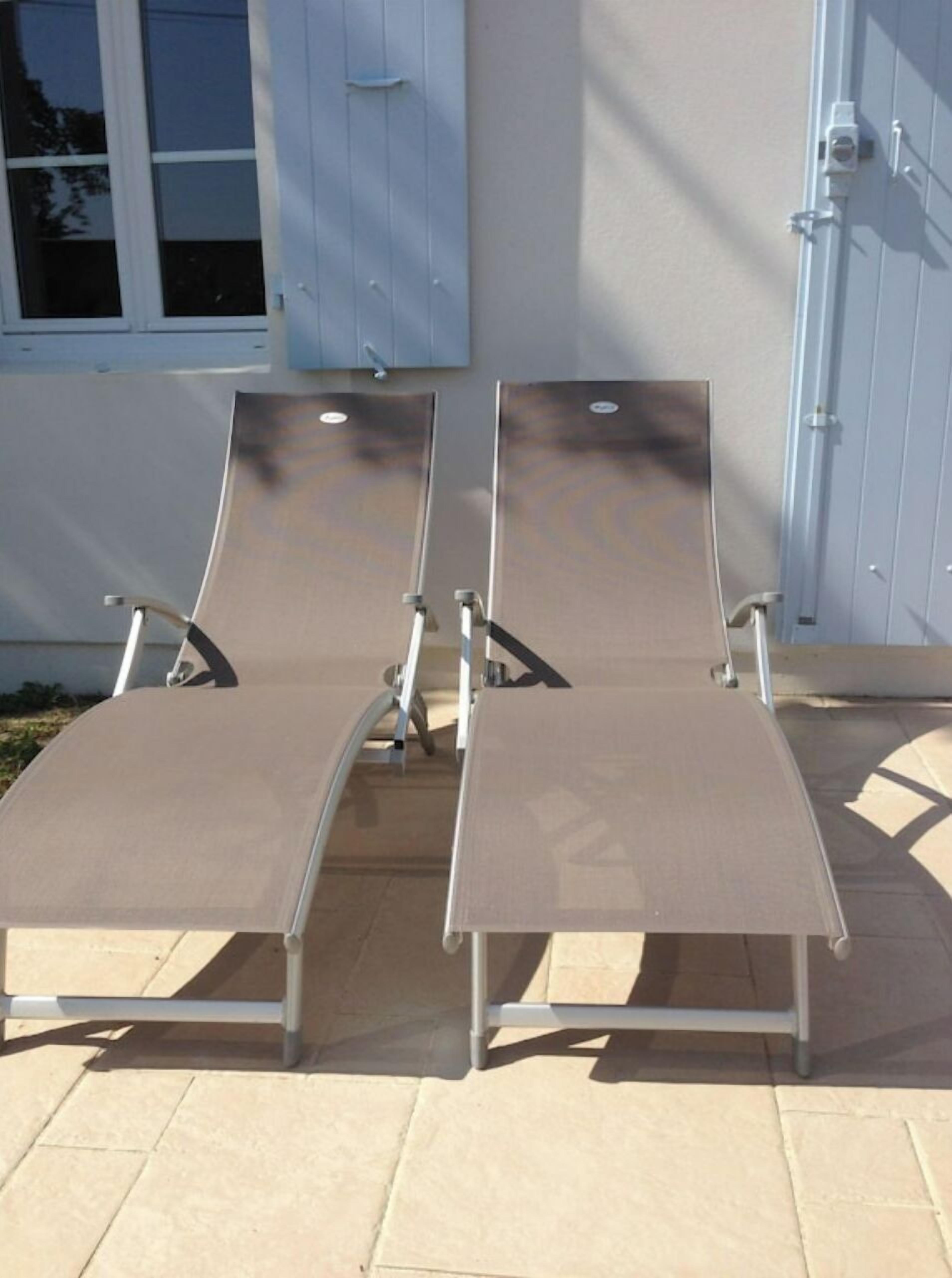 Two sun loungers with metal frames and fabric seats, positioned on a tiled patio area.