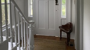 Ein helles Interieur mit einer Holztreppe, einer weißen Tür mit Fenster und einem braunen Stuhl.
