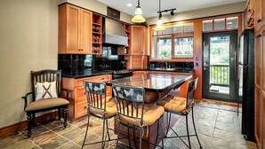 A spacious kitchen with a large island, wooden cabinets, and a dining area with bar stools. - Ski in/out! 4 bdrms,Blacksmith Lodge,views,heated garage,internet,8 pers hot tub (Beaverdell)