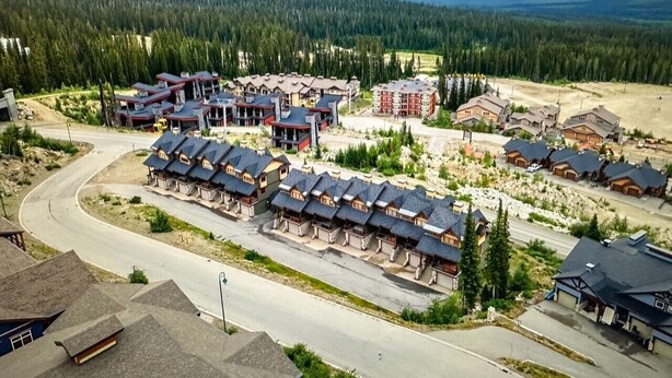 A residential area with multiple houses, a winding road, and a forested mountain range in the background. - Ski in/out! 4 bdrms,Blacksmith Lodge,views,heated garage,internet,8 pers hot tub (Beaverdell)
