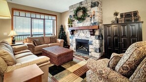 A cozy living room with a stone fireplace, a Christmas tree, and a large window with blinds. - Ski in/out! 4 bdrms,Blacksmith Lodge,views,heated garage,internet,8 pers hot tub (Beaverdell)