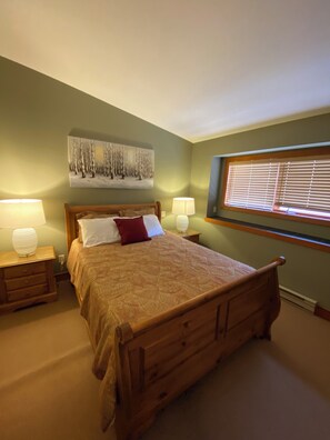 A bedroom with a wooden bed, two bedside tables with lamps, a window with blinds, and a painting on the wall. - Ski in/out! 4 bdrms,Blacksmith Lodge,views,heated garage,internet,8 pers hot tub (Beaverdell)