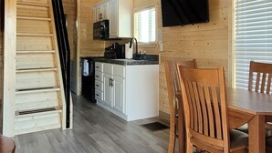 Interior de madera con escalera, un comedor con sillas de madera, una cocina con armarios blancos y un ventilador de techo.