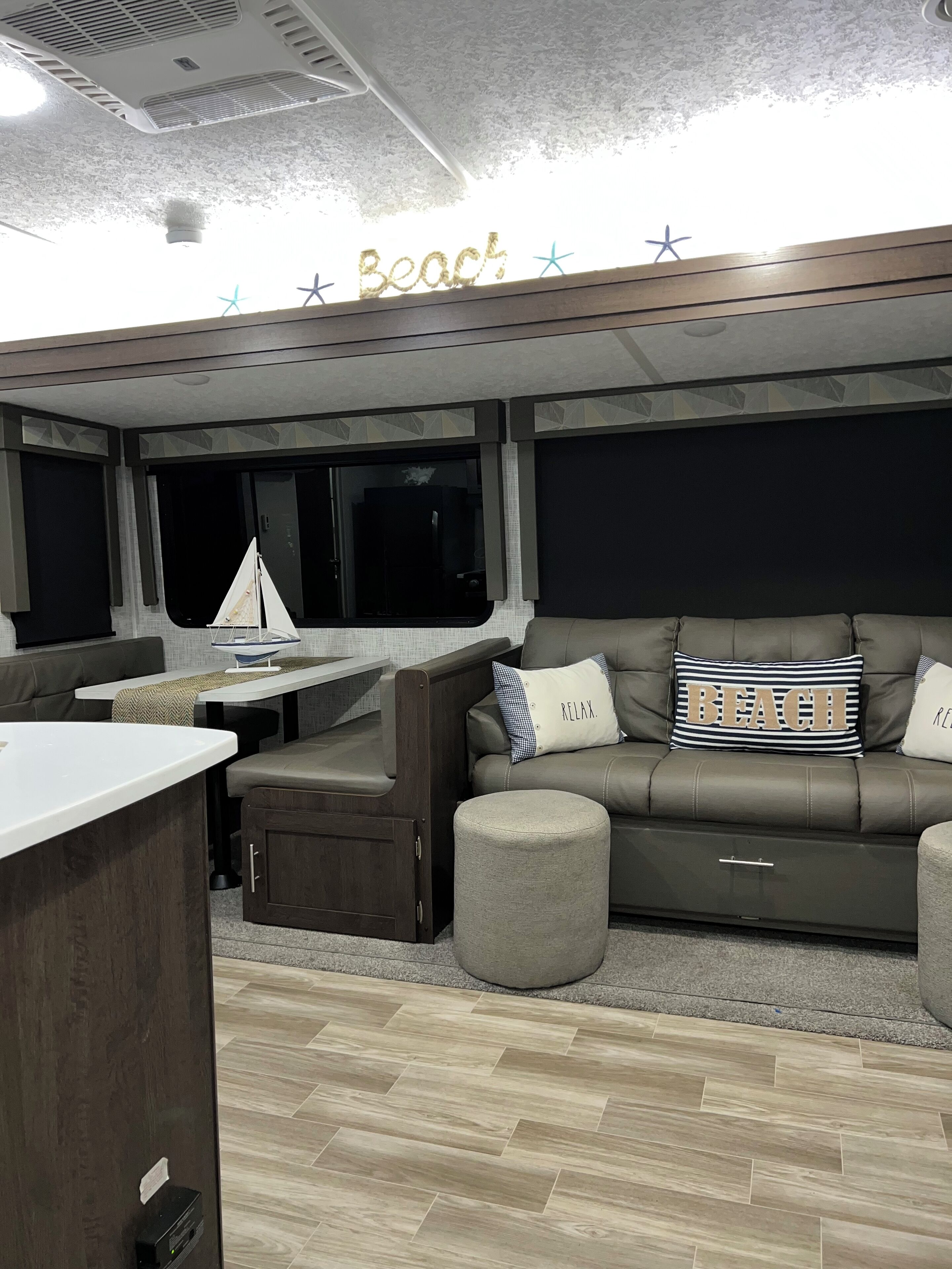 Un salon confortable avec un canapé, un pouf et une petite table. Une pancarte au-dessus indique : « Plage ».