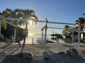 A beach with hammocks, a notice to renters, and a water body in the background.