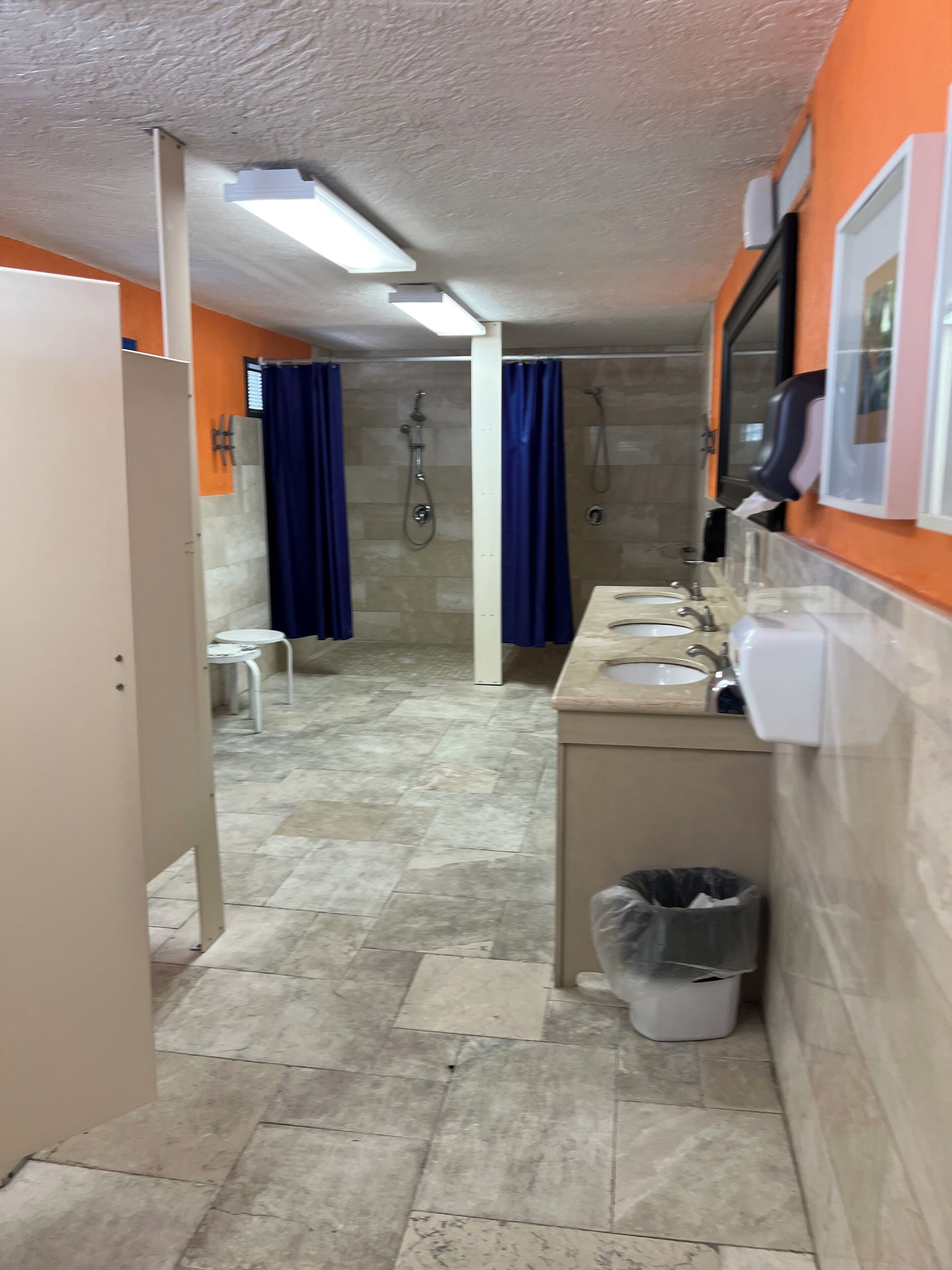 A narrow bathroom with a shower, a sink, and a trash bin.