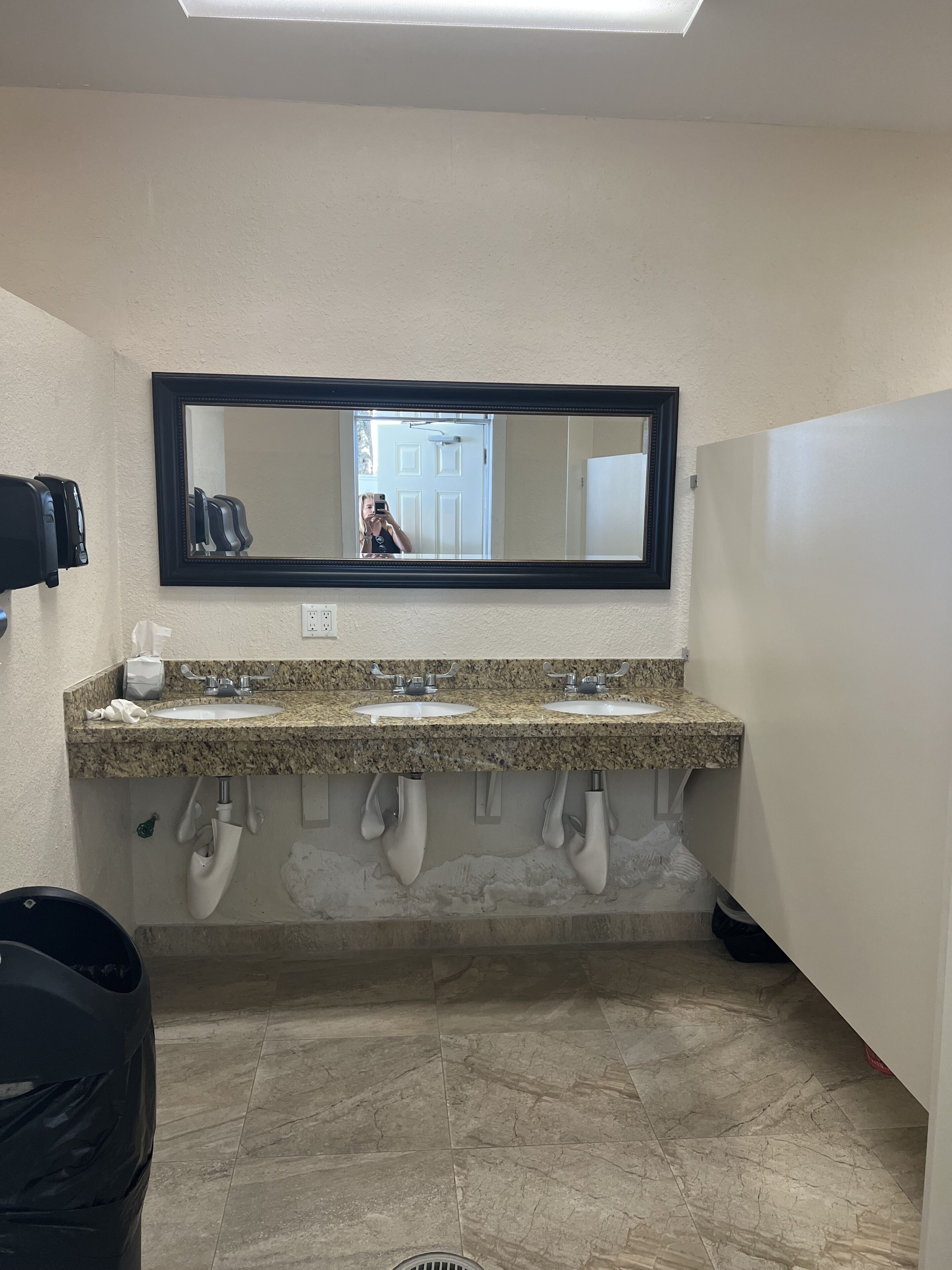 Un baño con dos lavamanos, un espejo grande y un bote de basura.