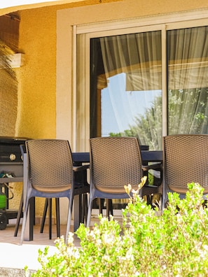 Une terrasse extérieure avec une table et des chaises, un barbecue et une fenêtre avec des rideaux.