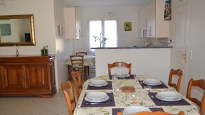 A dining area with a table set for four, chairs, a wooden cabinet, and a window with curtains. - 8-person villa with private pool at the foot of Mont Ventoux (Malaucène)