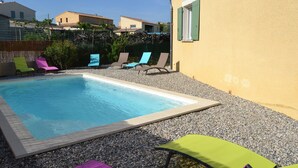 A rectangular swimming pool surrounded by pebbles, with colorful lounge chairs and a yellow building in the background. - 8-person villa with private pool at the foot of Mont Ventoux (Malaucène)