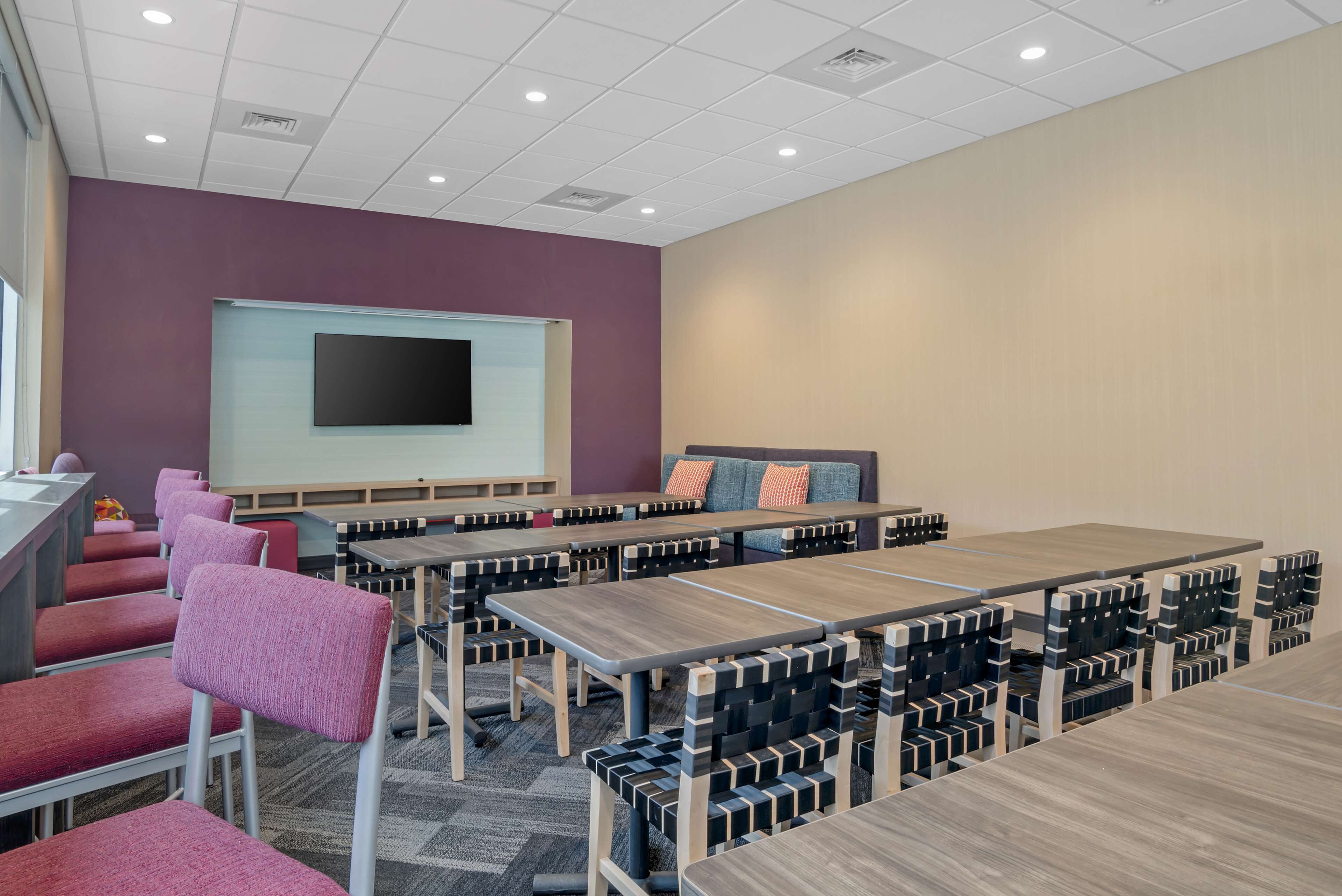 A conference room with multiple tables and chairs, a projector screen, and a sofa with pillows.