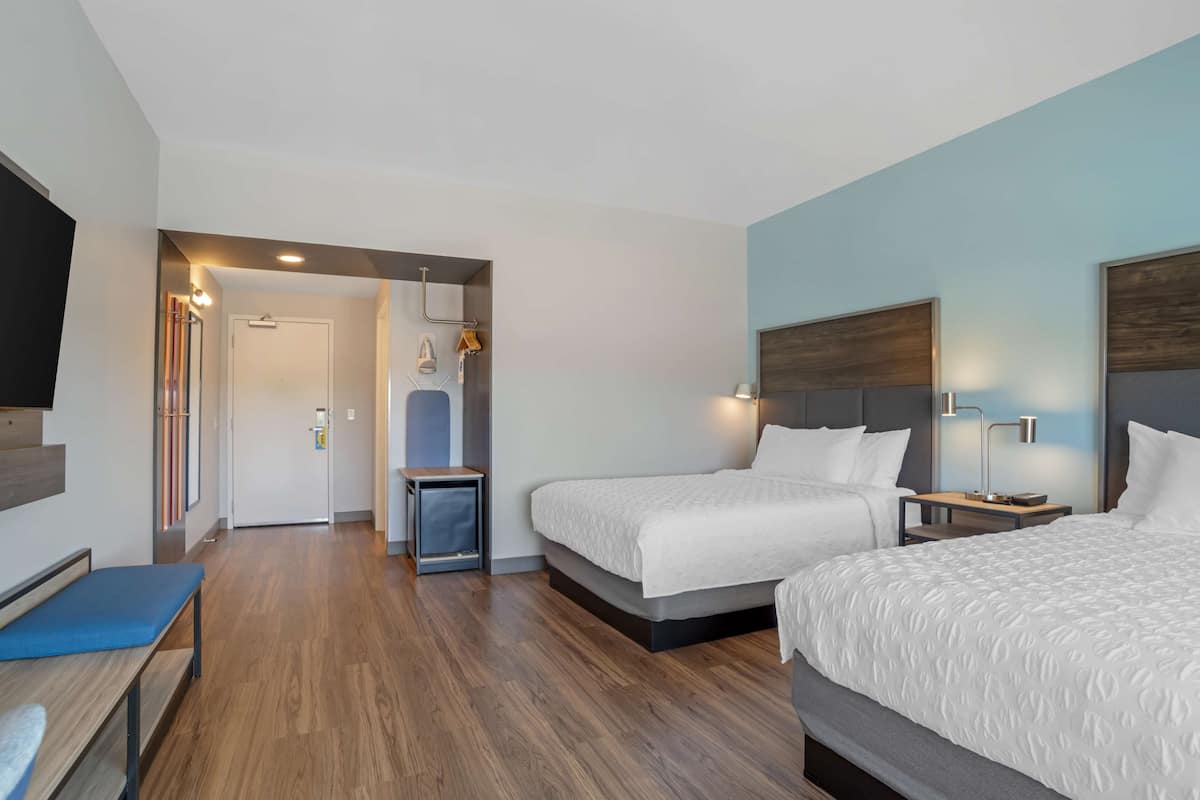 Ein Hotelzimmer mit zwei Betten, einem Schreibtisch, einer Bank und einem Fernseher.