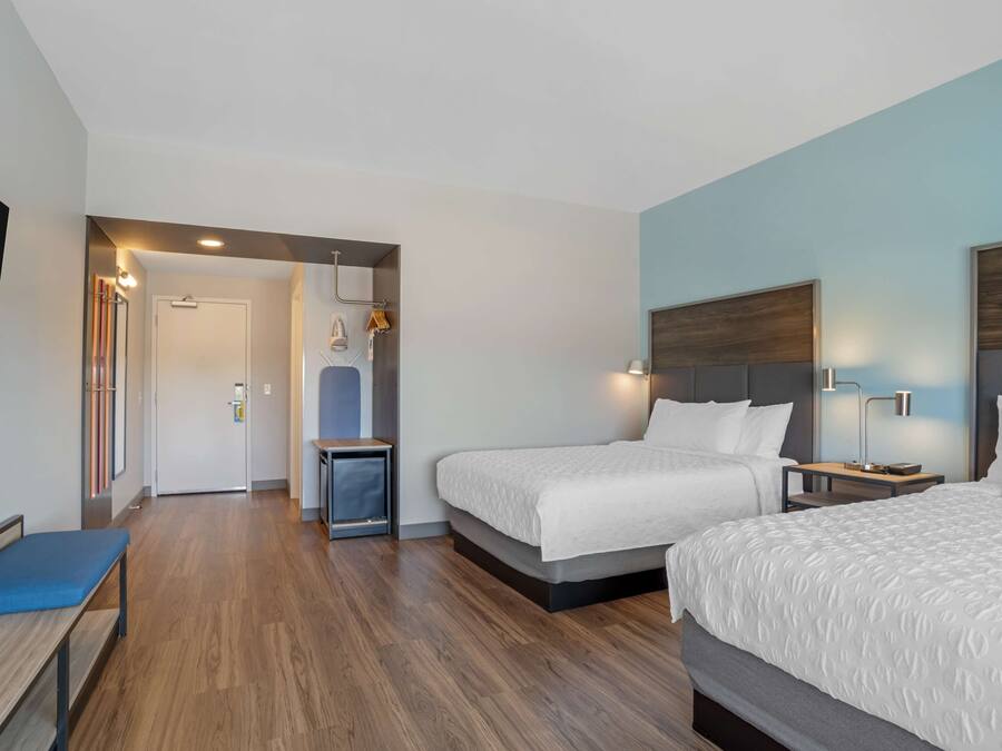 Una habitación de hotel con dos camas, un escritorio, un banco y un televisor.