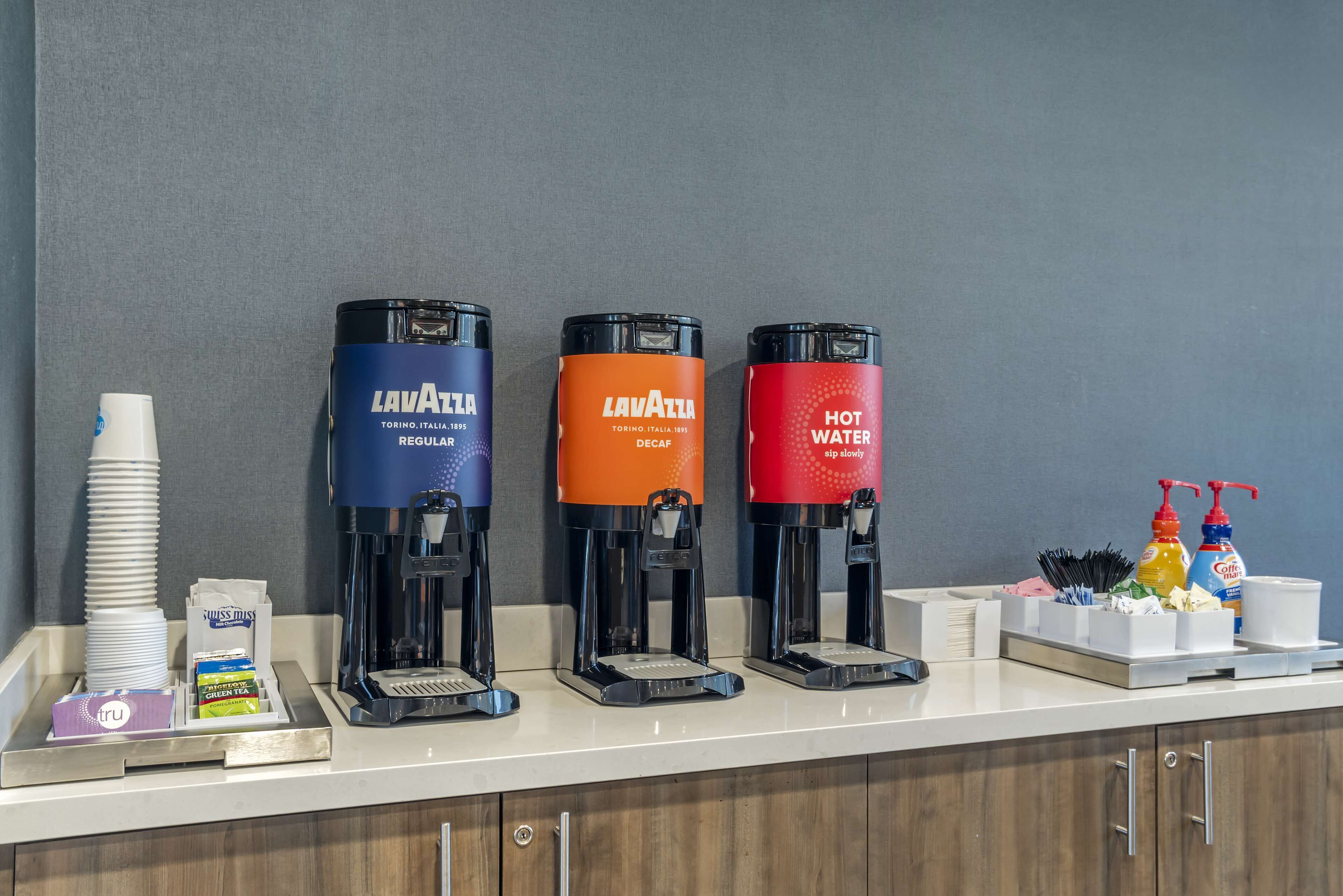 Trois machines à café de la marque « LAVATTA », chacune offrant différentes options de température de l’eau, une pile de tasses blanches et un espace dédié au café, équipé de divers accessoires.