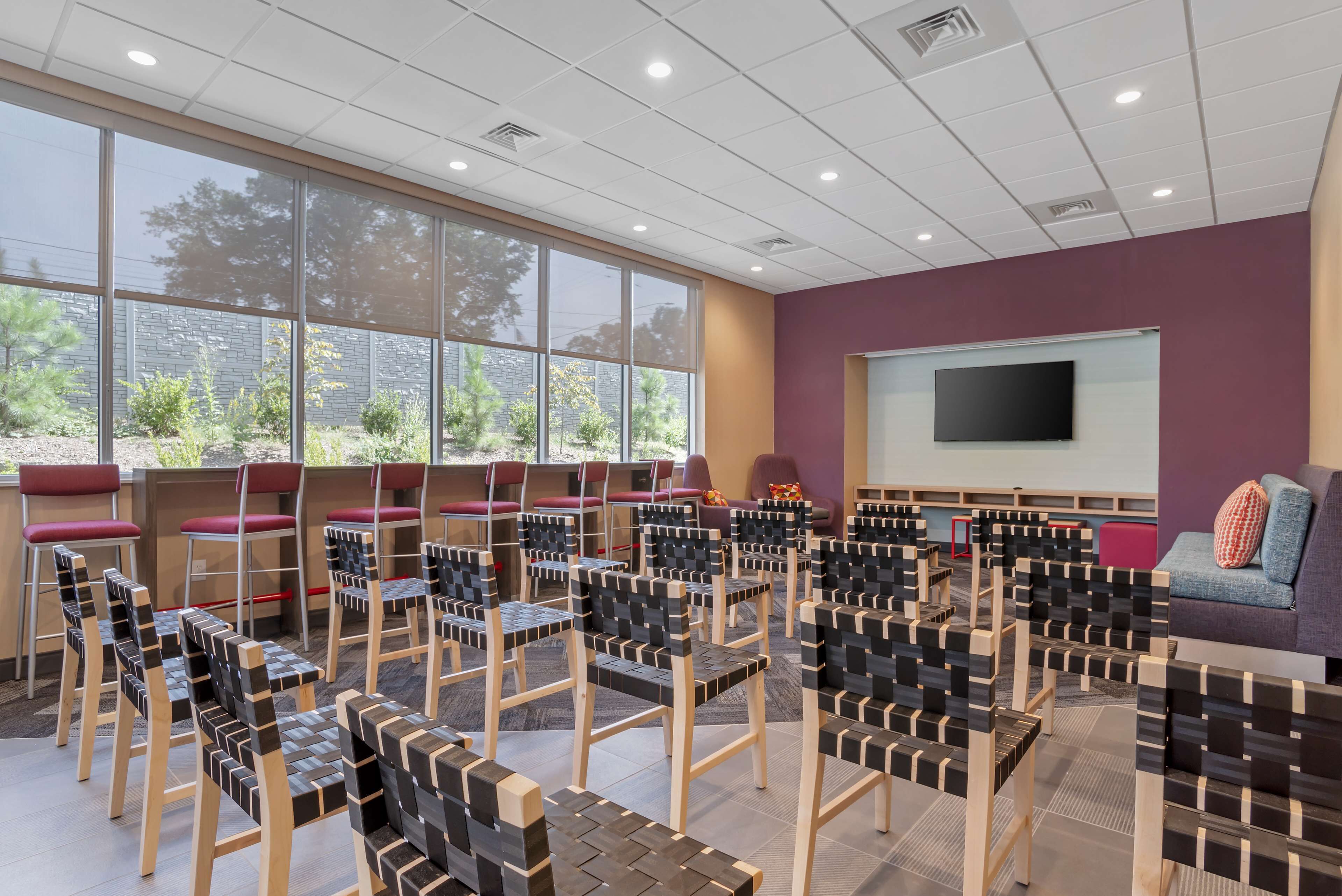 A conference room with rows of chairs, a large screen, and a window with a view of trees.