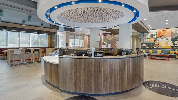 Un'accogliente area reception di un hotel moderno, con una scrivania in legno, un lampadario a soffitto circolare e un angolo salotto con divano e poltrone.
