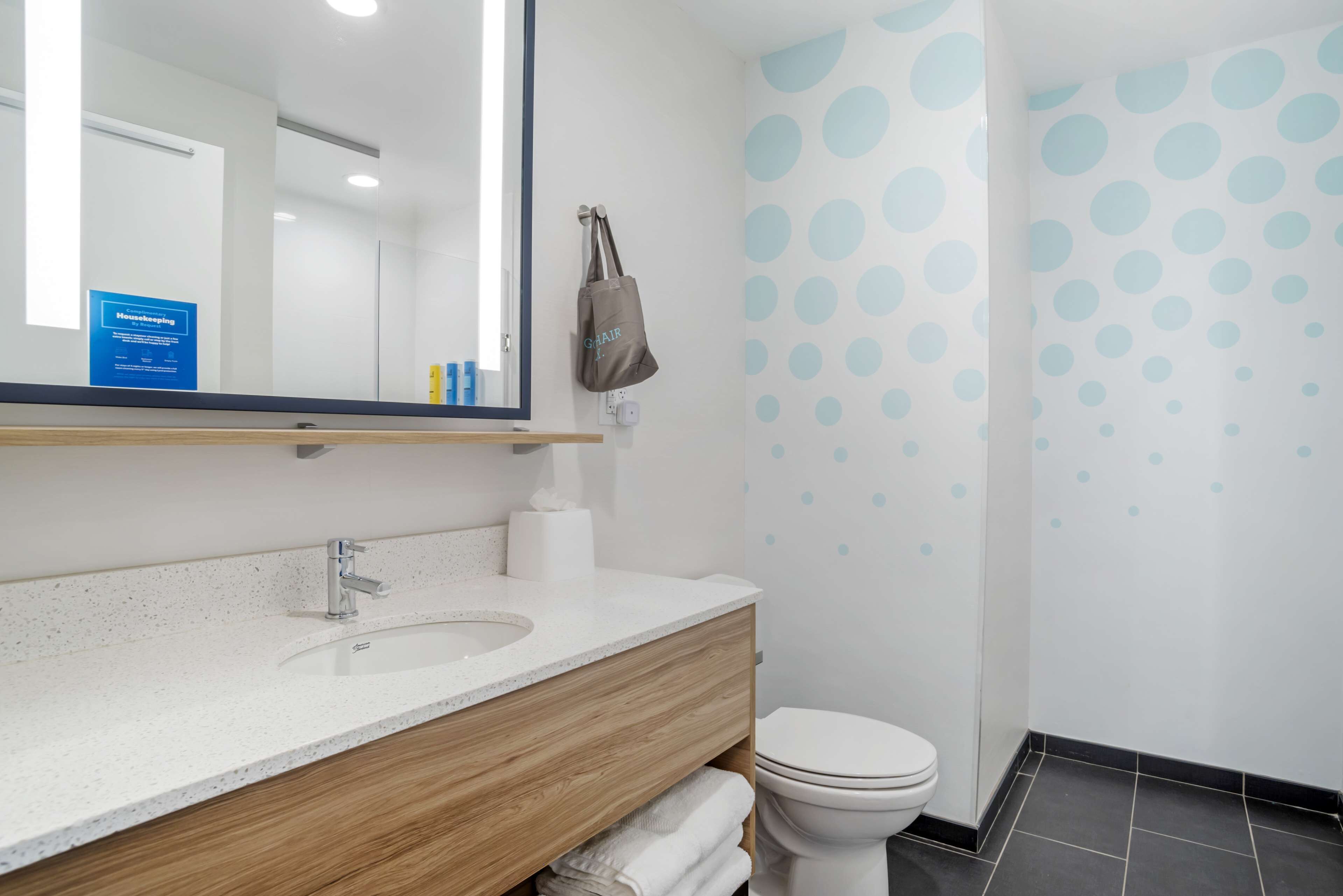 A modern bathroom with a wooden vanity, a sink, a toilet, and a mirror.