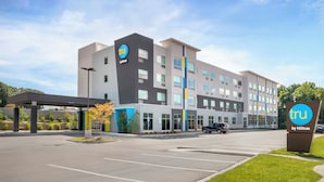 Un moderno edificio di un hotel con un cartello ben visibile 'tru by Hilton', un'area di parcheggio coperta e un cielo sereno.