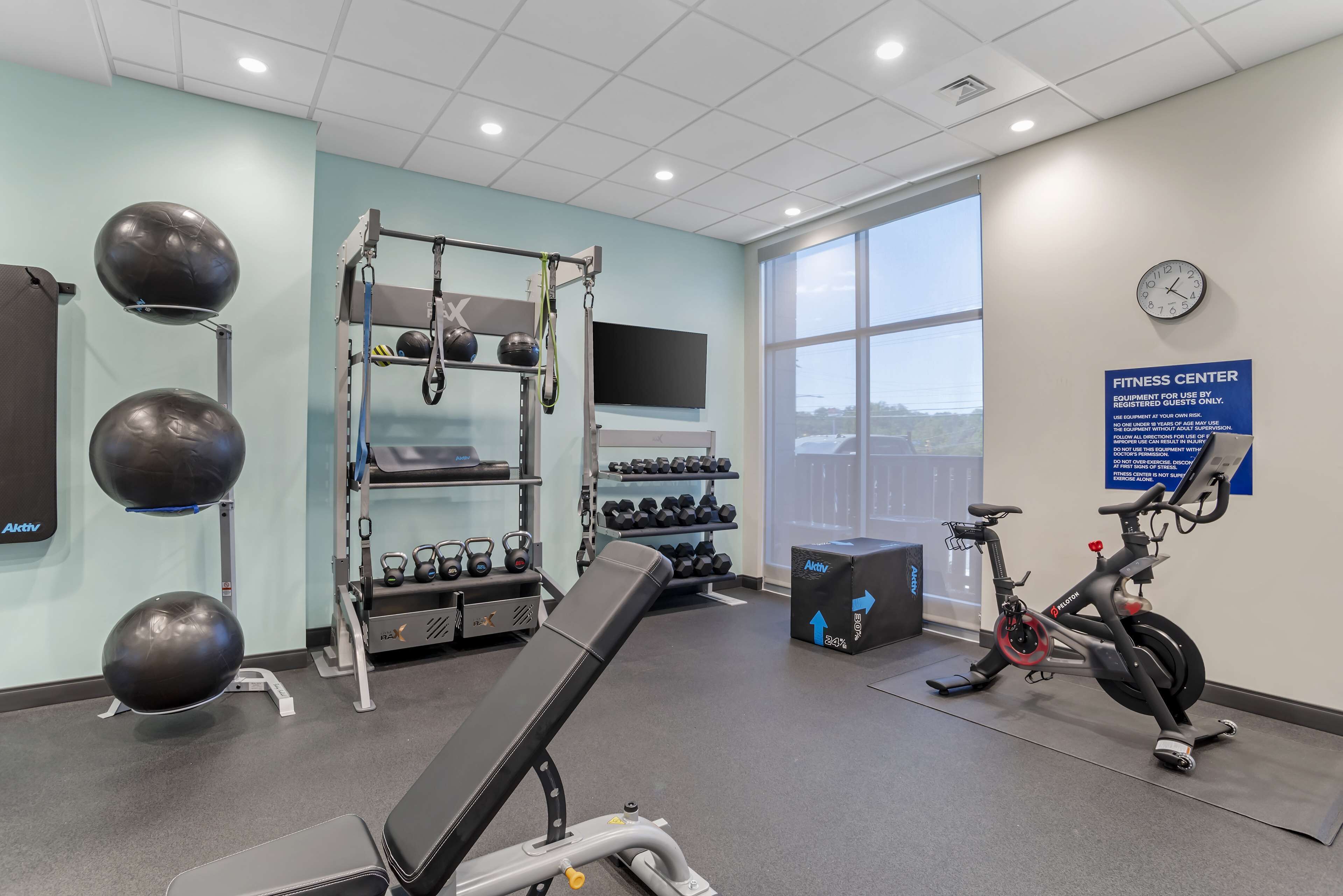 A fitness center with exercise equipment, a wall-mounted TV, and a large window offering a view.