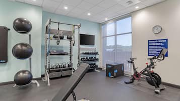 A fitness center with exercise equipment, a wall-mounted TV, and a large window offering a view.