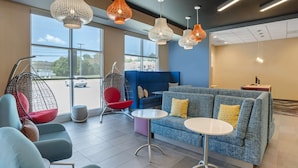 Una moderna area lounge con lampade a sospensione, un divano blu con cuscini gialli, una poltrona rossa e una poltrona a forma di uovo.
