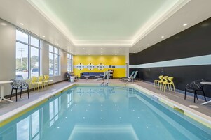 Una piscina con paredes amarillas y negras, rodeada de sillas y mesas amarillas.