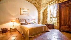Een slaapkamer met een stenen plafond, een bed met een witte dekbedovertrek, een nachtkastje met een lamp en een houten garderobe.