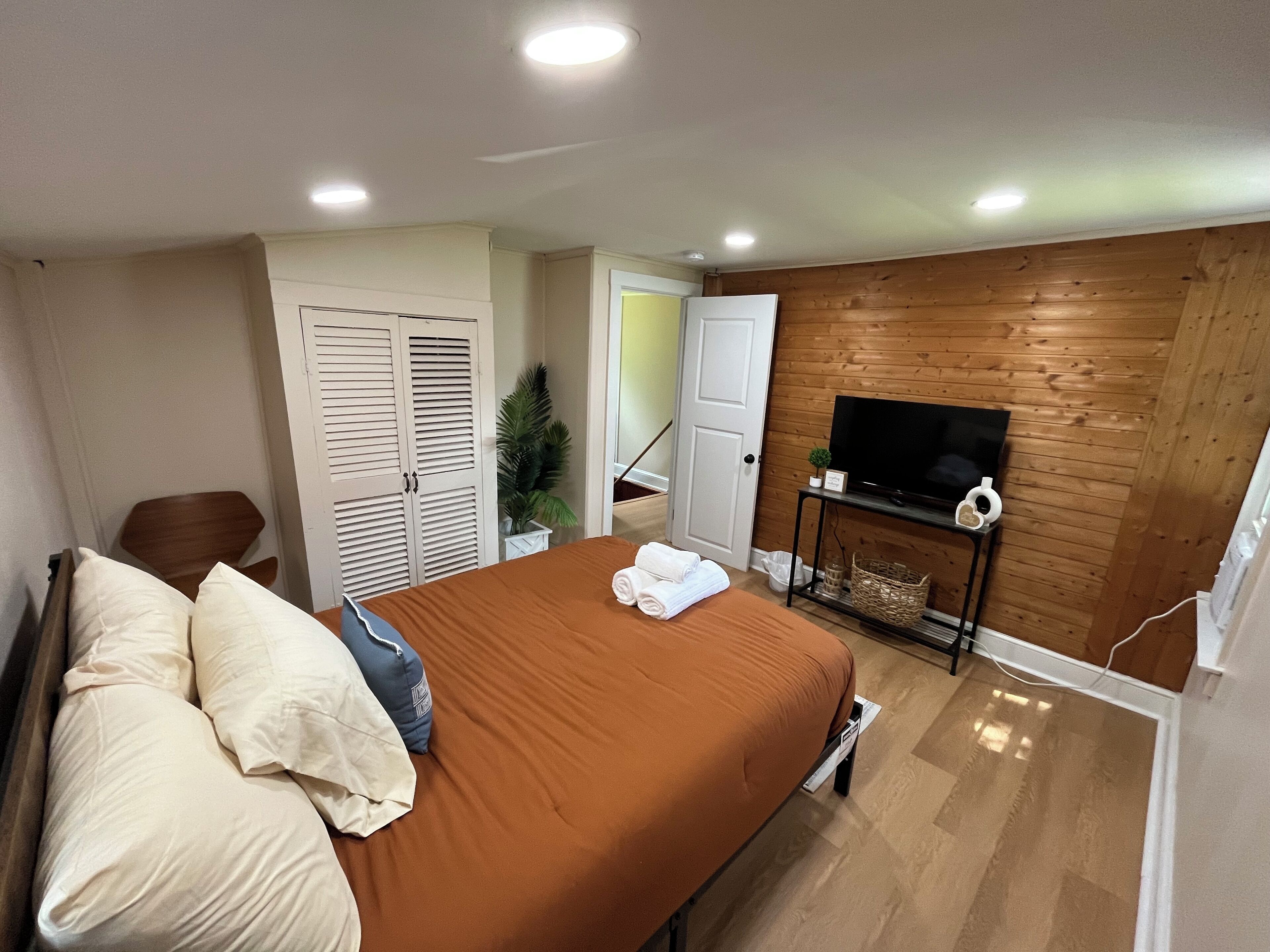 A bedroom with a bed, a TV, a wooden wall, and a door.