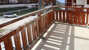 A balcony with wooden railings overlooking a street with parked cars and a building in the background. - Floor -1, view ski slopes, swimming pool, sauna, balcony, tv, ski locker, 29m², Les Orres (Les Orres)