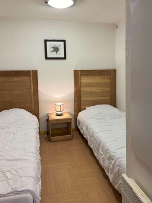 A small, clean room with two beds, a bedside table with a lamp, and a framed picture on the wall.