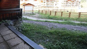 A view from a balcony with a wooden railing, a gravel path, and a wooden fence. In the background, there are buildings with balconies and a mountainous landscape. - Floor -1, view ski slopes, swimming pool, sauna, balcony, tv, ski locker, 29m², Les Orres (Les Orres)