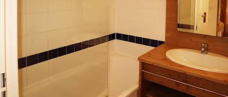 A bathroom with a bathtub, a wooden vanity with a sink, and a mirror.