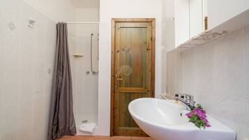 Een badkamer met een houten deur, een douche, een wastafel met bloemversiering en een toilet.