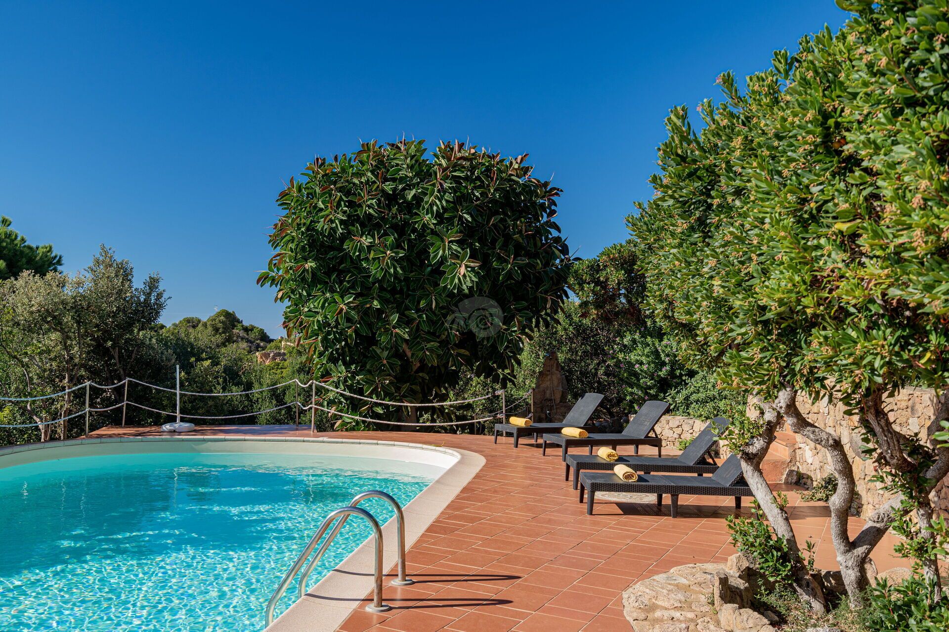 A poolside area with a clear blue pool, lounge chairs, and a stone wall.
