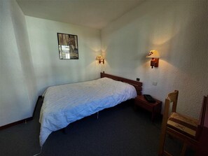 Simple hotel room with a single bed, nightstand, and chair, featuring a framed picture above the bed.