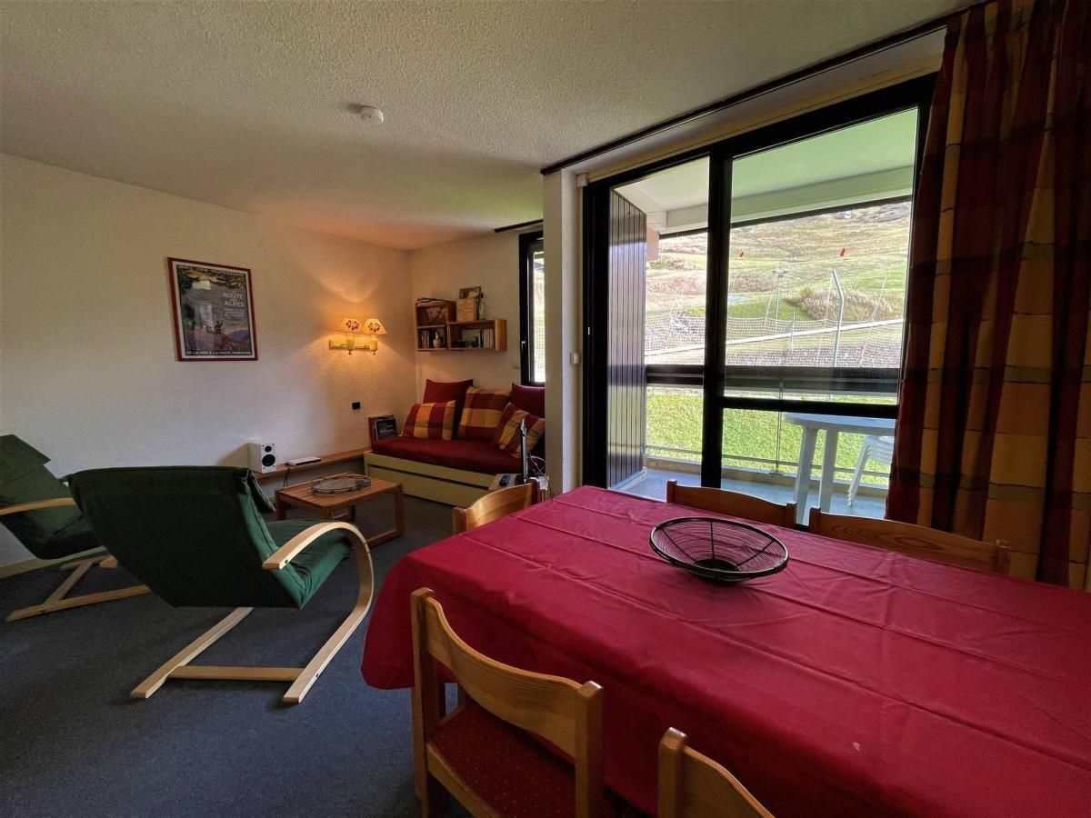 Una habitación con una mesa de comedor, sillas, un sofá, un sillón verde, una mesita con una lámpara y una ventana con vistas al exterior.