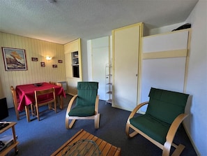 A room with a dining table, two green cushioned chairs, a wooden coffee table, and a bookshelf. - 300m from resort center, 3rd floor, balcony, tv, ski locker, 40m², Les Menuires (Les Menuires)