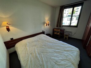 Habitación de hotel con una cama individual, dos lámparas de pared, un escritorio pequeño y una ventana con cortinas.
