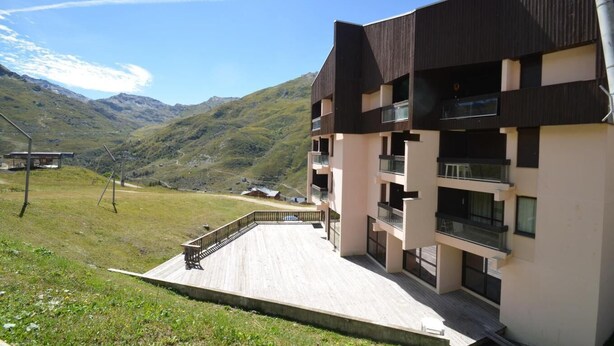 Un bâtiment moderne doté de nombreux balcons, d’une terrasse en bois et surplombant un paysage montagneux.