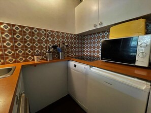 Compact kitchen with a modern design, featuring a dishwasher, microwave, and geometric tile backsplash.